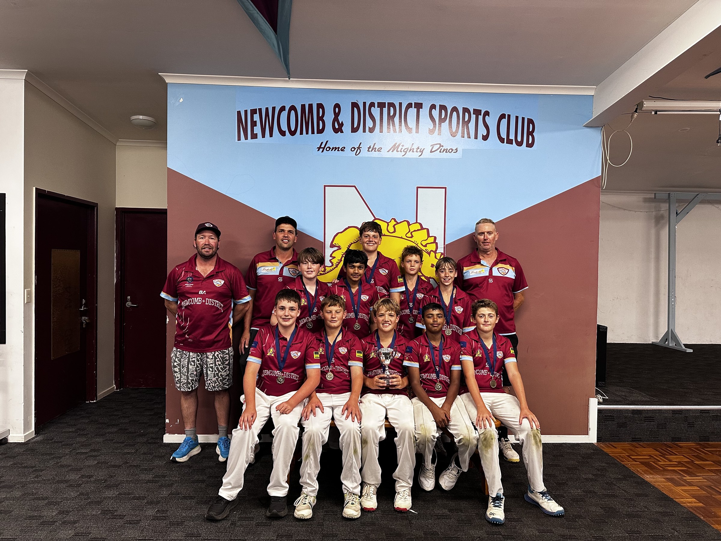 NDCC junior premiership team displaying medals and trophies beneath the club banner.