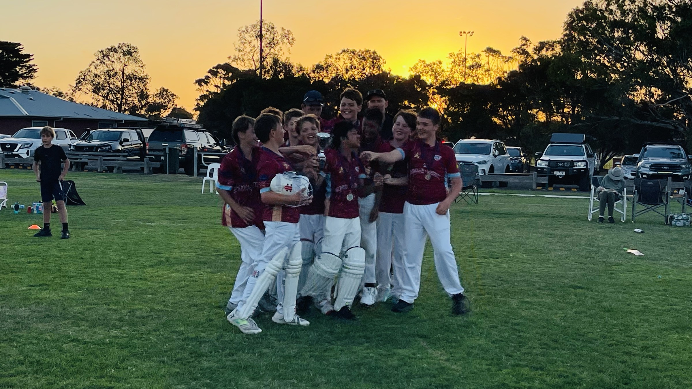 NDCC Under 13 players celebrating together on the oval at sunset.