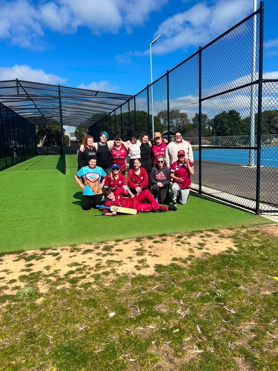 NDCC junior players in maroon kit posing beside the practice nets.