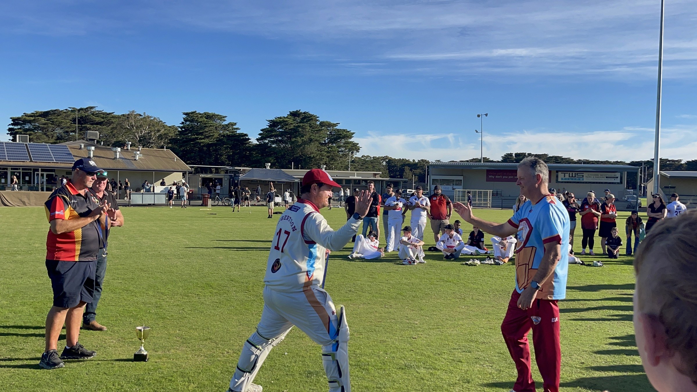 NDCC cricketers in whites greeting teammates and supporters on the oval after the grand final.