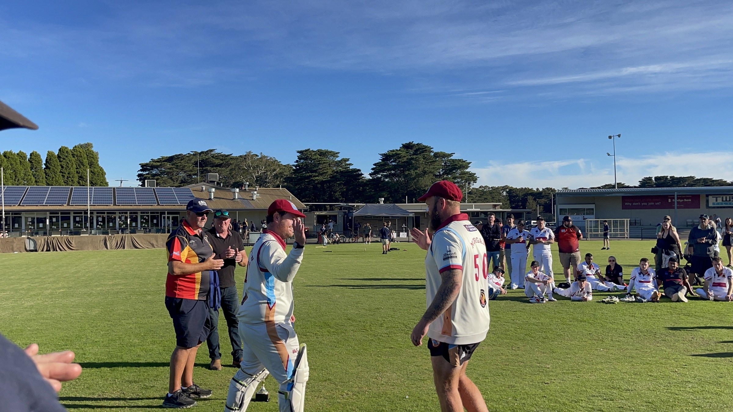 NDCC cricketers in whites greeting teammates and supporters on the oval after the grand final.