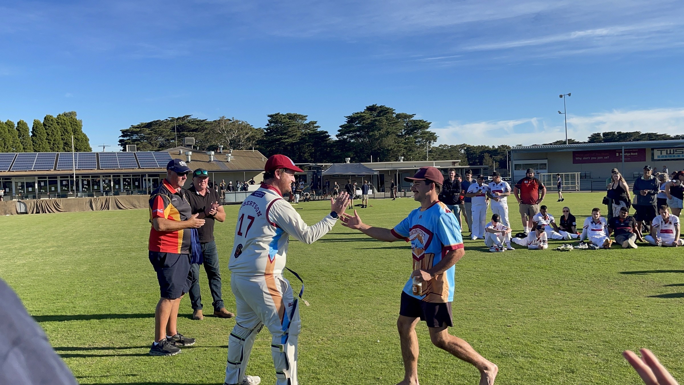 NDCC cricketers in whites greeting teammates and supporters on the oval after the grand final.