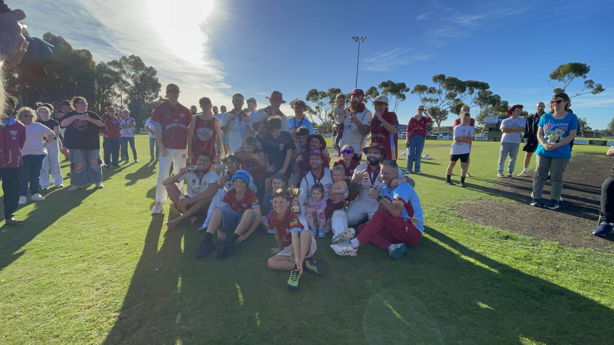 NDCC players in cricket whites and supporters posing together after the premiership win.