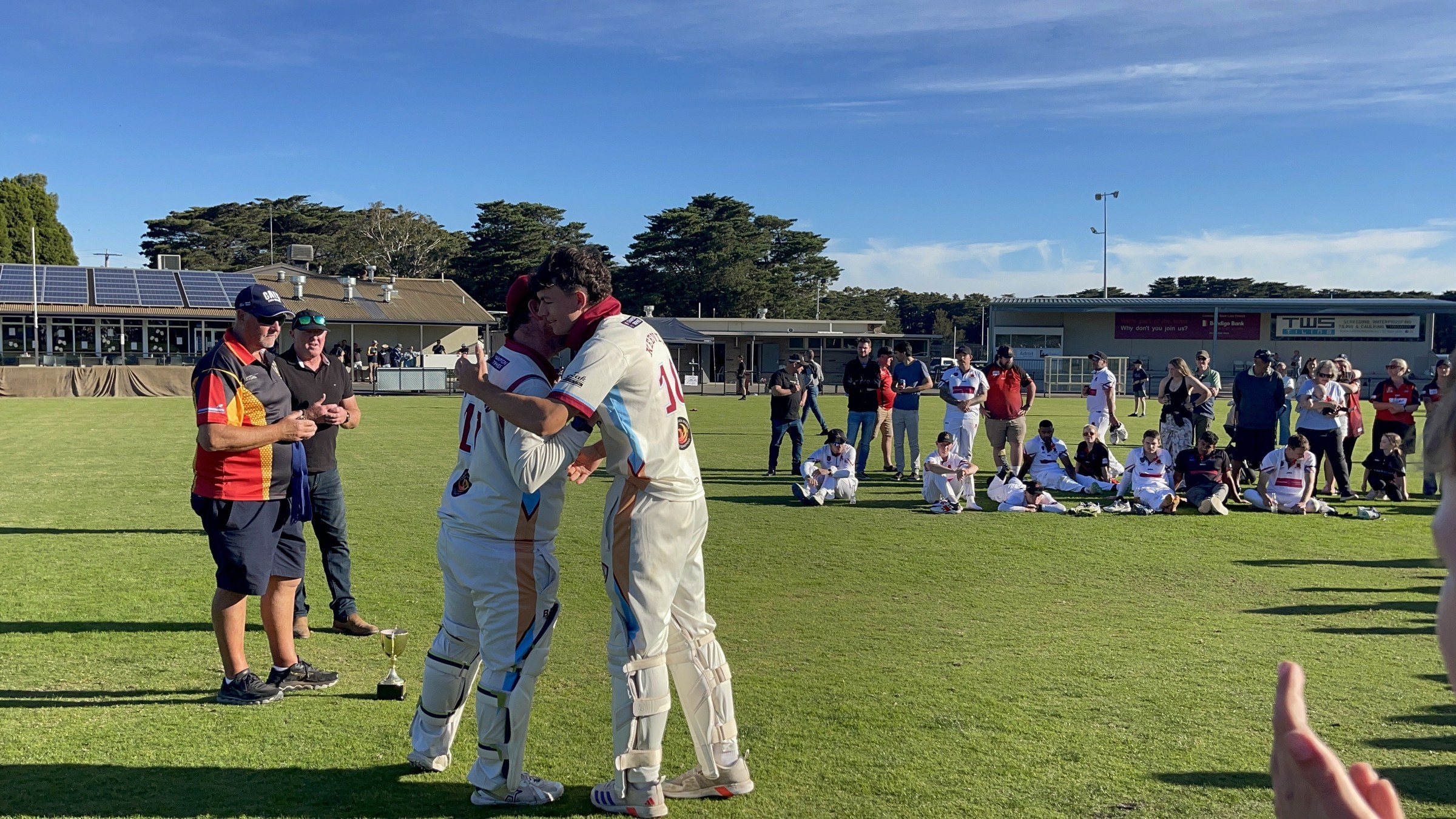 NDCC cricketers in whites greeting teammates and supporters on the oval after the grand final.