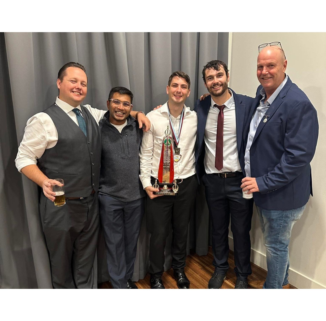 Five club members dressed for presentation night, posing together in front of grey curtains.